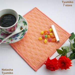 Può includere: Un sottopentola trapuntato color pesca con un motivo geometrico. Il sottopentola è circondato da una tazza di caffè, un piatto, una piccola scatola e alcuni dolci colorati. Il testo "Natasha Tyumiko" appare nell'immagine.