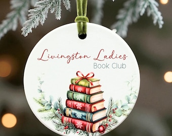 May include: Round white Christmas ornament with the text "Livingston Ladies Book Club" in red script. The ornament features a stack of books with a red bow, surrounded by greenery and a red ornament.