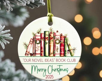 May include: A round Christmas ornament with a green ribbon. The ornament features a stack of books decorated with wreaths and bows. Text on the ornament reads "OUR NOVEL IDEAS BOOK CLUB" and "Merry Christmas 2025".