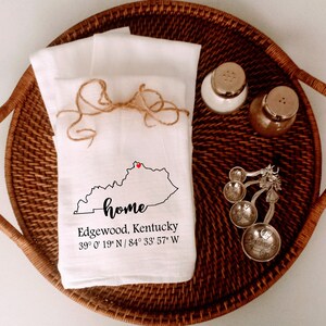 May include: White kitchen towel with a black outline of the state of Kentucky and the word "home" written in cursive. A red heart is placed on the state outline. The text "Edgewood, Kentucky 39° 0' 19" N / 84° 33' 57" W" is printed below the state outline.