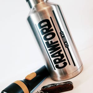 May include: A stainless steel water bottle with a black handle and the word "CRAWFORD" printed on the side. The bottle is next to a flashlight, a multi-tool, and a set of keys.