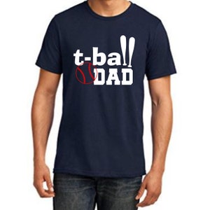 May include: A navy blue t-shirt with white text that reads "t-ball DAD" and a red and white baseball graphic.