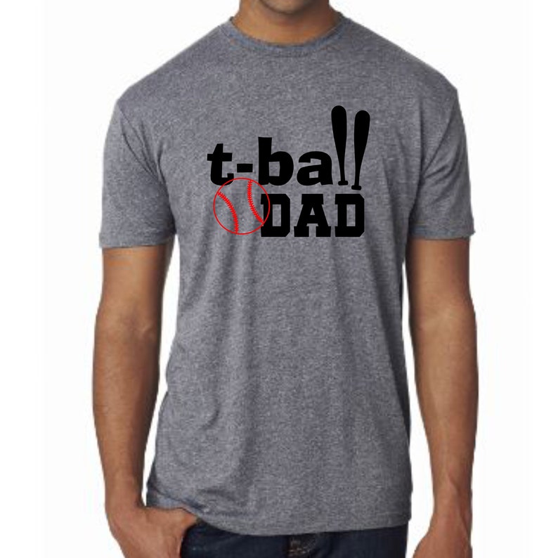 May include: A heather grey t-shirt with black text that reads "t-ball DAD" and a red baseball graphic.