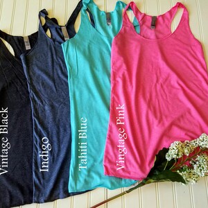 May include: Four tank tops in different colors: indigo, vintage black, vintage pink, and Tahiti blue. The tank tops are laid out on a white surface with a white flower stem.