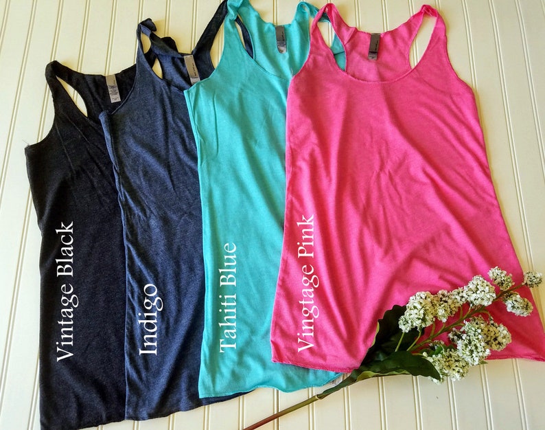 May include: Four tank tops in different colors: indigo, vintage black, vintage pink, and Tahiti blue. The tank tops are laid out on a white surface with a white flower stem.