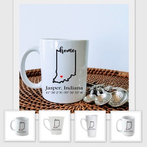 May include: White ceramic mug with a black outline of the state of Indiana and the word "home" in cursive. The mug also has the text "Jasper, Indiana 41° 36' 2" N / 93° 36' 32" W" printed on it.