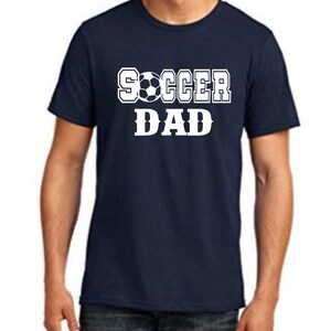 Puede incluir: Una camiseta azul marino con texto blanco que dice "SOCCER DAD" con un gr&aacute;fico de bal&oacute;n de f&uacute;tbol.