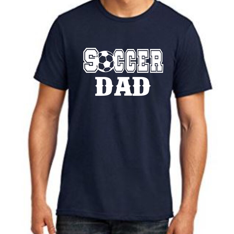 Puede incluir: Una camiseta azul marino con texto blanco que dice "SOCCER DAD" con un gr&aacute;fico de bal&oacute;n de f&uacute;tbol.