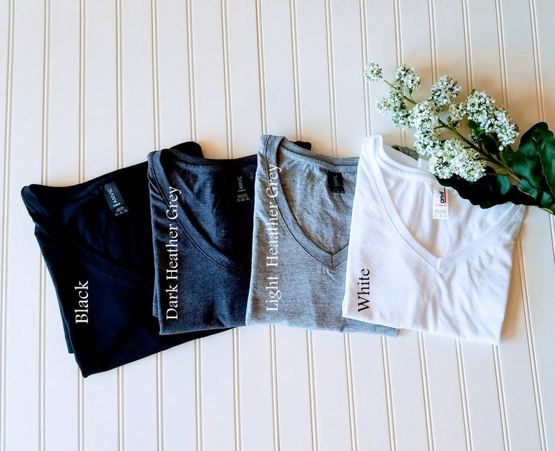 K&ouml;nnte beinhalten: Vier V-Ausschnitt-T-Shirts in verschiedenen Farben: Schwarz, Dunkelgrau meliert, Hellgrau meliert und Wei&szlig;. Jedes Shirt hat ein Etikett mit dem aufgedruckten Farbnamen.