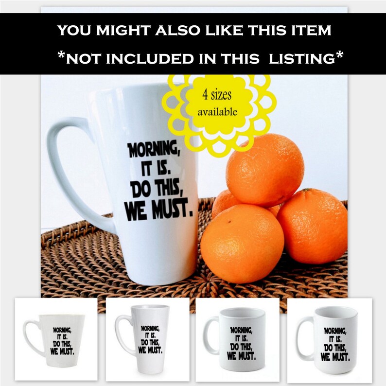 May include: White ceramic mug with the text "Morning, It Is. Do This, We Must." in black lettering. The mug is on a woven brown surface with four oranges in the background.