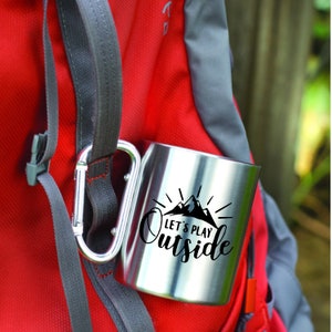May include: A stainless steel travel mug with a black graphic that says "Let's Play Outside" and a mountain range with a sunburst behind the text.
