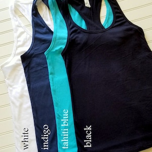 May include: Three racerback tank tops in white, indigo blue, and black. The tank tops are layered on top of each other, with the white tank top on the bottom and the black tank top on the top. The tank tops are all made of a soft, comfortable fabric.