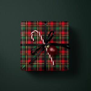 A gift box wrapped in a red and black plaid pattern, tied with a black ribbon, and adorned with a candy cane and a red ornament.