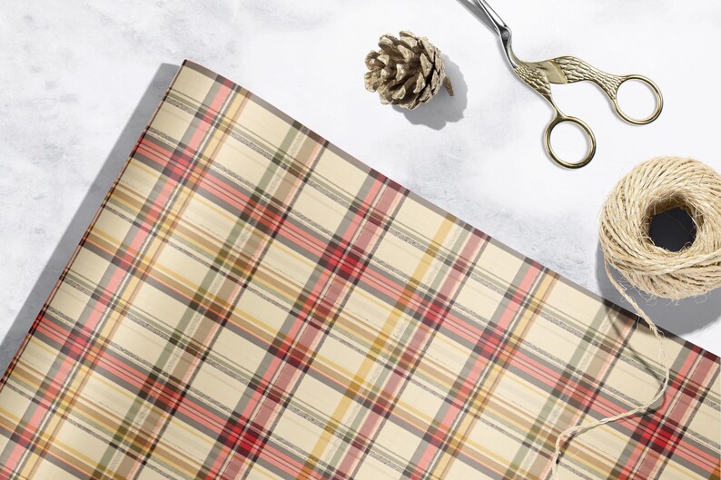 a plaid wrapping paper, a pair of scissors, a pine cone, and a spool of twine or string, all arranged on a white surface.