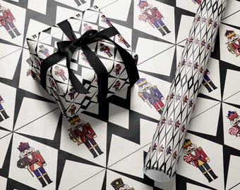 May include: A wrapped gift box with a black satin ribbon and a roll of wrapping paper. The wrapping paper features a repeating pattern of colourful nutcracker illustrations on a white background with a black geometric design.