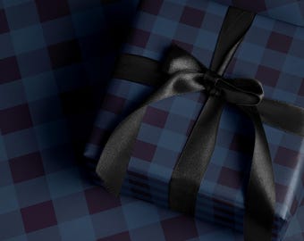 Puede incluir: Un regalo envuelto en papel a cuadros azul marino y burdeos, adornado con una cinta y un lazo de satén negro. El regalo se presenta sobre una superficie a cuadros a juego, creando una estética elegante.