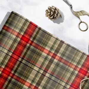 a plaid fabric with a red and green pattern, along with a pair of scissors, a pine cone, and some string or yarn.