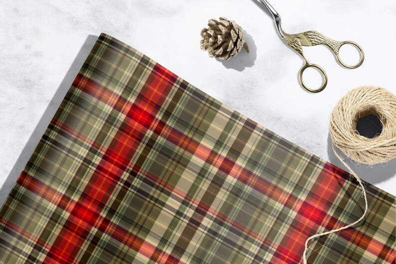 a plaid fabric with a red and green pattern, along with a pair of scissors, a pine cone, and some string or yarn.