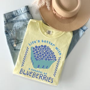 a yellow shirt with blueberries on it next to a straw hat