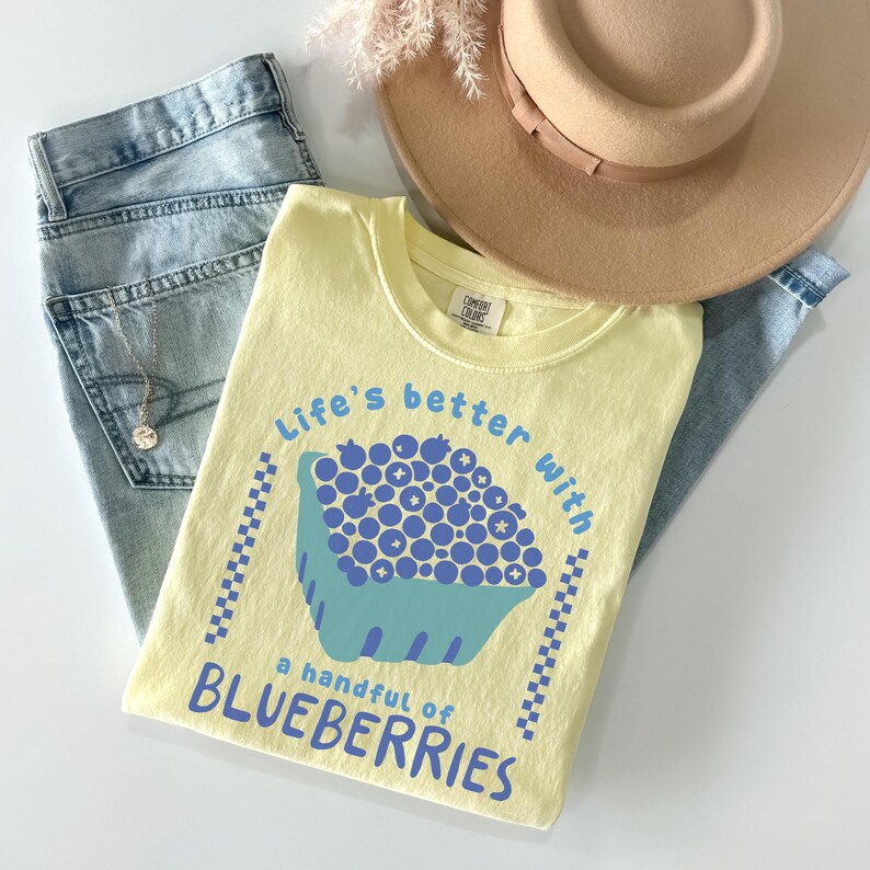 a yellow shirt with blueberries on it next to a straw hat
