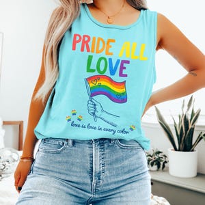 Puede incluir: Una camiseta sin mangas azul claro con las palabras "PRIDE ALL LOVE" en colores arcoíris. La camiseta presenta una bandera arcoíris con corazones y la frase "love is love in every color."