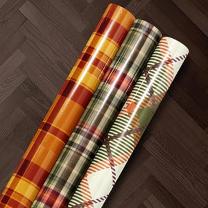Three rolls of colorful, patterned wrapping paper are arranged on a wooden floor.