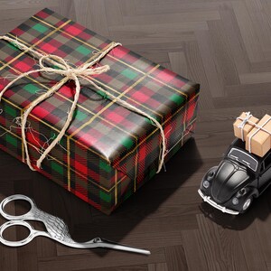A red and green plaid gift box with a bow, a pair of scissors, and a small toy car on a wooden floor.