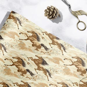 a beige and brown patterned wrapping paper with a horse design, along with a pair of scissors, a pine cone, and some string or twine.