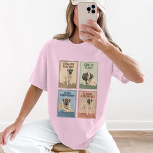 Op de afbeelding: Een lichtroze t-shirt met vier ingelijste afbeeldingen van Engelse Mastiff-honden. Elke afbeelding heeft een ander onderschrift: "English Mastiff", "Gentle Giant", "Loyal Companion" en "Strong & Steadfast".