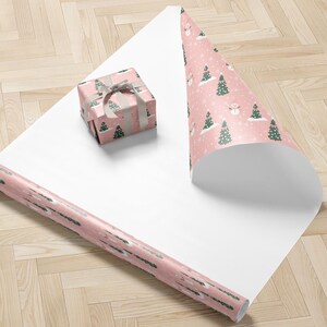A pink and white Christmas-themed gift wrapping paper with a snowman and pine trees on it, along with a small gift box wrapped in the same paper.