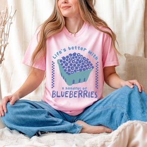 a woman sitting on a bed wearing a pink shirt