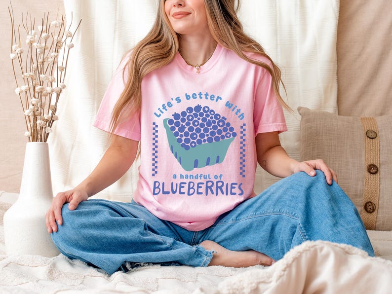 a woman sitting on a bed wearing a pink shirt