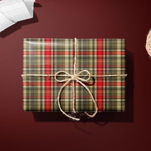 a gift box wrapped in a plaid pattern, tied with a twine bow, and accompanied by a pair of scissors and a spool of twine on a dark red background.