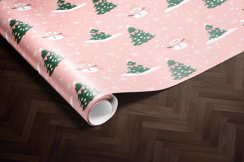A roll of pink wrapping paper with a repeating pattern of Christmas trees and snowmen on it, placed on a wooden floor.