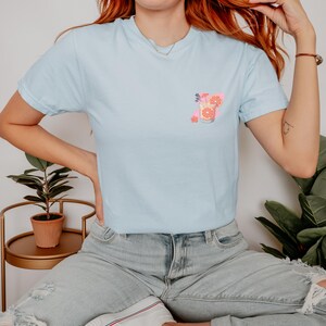 a woman with red hair wearing a blue shirt and ripped jeans