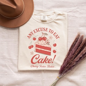 a t - shirt with a cake on it next to a straw hat