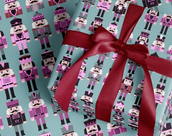 May include: Gift wrap with a repeating pattern of toy nutcracker soldiers in pink, purple, grey, and black on a teal background. A burgundy ribbon is tied in a bow around the wrapped gift.