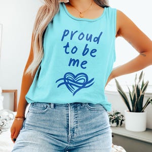 Peut inclure: Un débardeur bleu clair avec l'inscription "proud to be me" en bleu foncé. En dessous, un motif de cœur bleu foncé. Le haut est sans manches et fabriqué dans une matière douce.