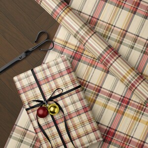 a wrapped gift with a plaid pattern, a pair of scissors, and a ribbon with a red ornament on a wooden surface.