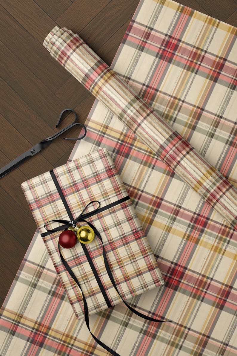 a wrapped gift with a plaid pattern, a pair of scissors, and a ribbon with a red ornament on a wooden surface.