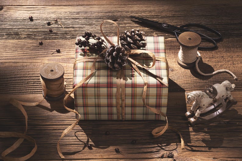 A gift wrapped in a plaid paper with pine cones and a small toy horse on a wooden table.