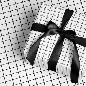 May include: A present wrapped in white paper with a black grid pattern, tied with a black satin ribbon. The background mirrors the grid design. The bow is centrally placed, adding a touch of elegance to the gift.
