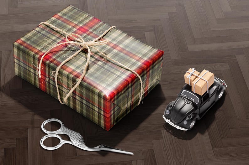 A gift box wrapped in a plaid paper with a bow, a pair of scissors, and a small toy car on a wooden floor.