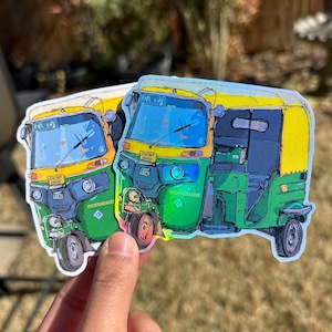 May include: A sticker featuring two colorful auto rickshaws, a common mode of transport in India. The vehicles are primarily green, yellow, and blue, with the text "HYDERABADIE" and "KHOWP 6845K" visible. The sticker has a holographic finish.