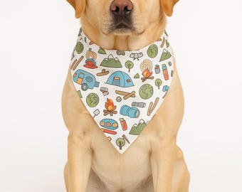 May include: A yellow Labrador Retriever sits, wearing a white bandana. The bandana features a camping-themed pattern with illustrations of tents, campfires, trees, and RVs. The dog is centered against a white background.