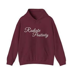 Könnte beinhalten: Ein weinroter Hoodie mit einer weißen, kursiv geschriebenen Aufschrift "Radiate Positivity".