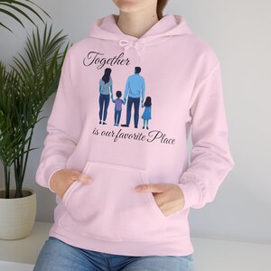May include: Pink hoodie featuring a graphic of a family of four holding hands and the text "Together is our favourite place".