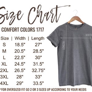 May include: A gray Comfort Colors 1717 t-shirt hanging on a wooden hanger. The image includes a size chart with measurements in inches for sizes S through 4XL. The chart shows width and length measurements for each size.