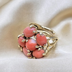 May include: A gold-toned ring featuring a cluster of oval, coral-colored stones. The ring's design incorporates delicate, branch-like structures that cradle each stone, creating a unique and eye-catching piece of jewelry.