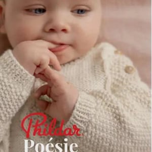May include: A close-up of a baby wearing a white knitted sweater with the text "Phildar Poésie Miniature" in red. The baby is looking at the camera and has a finger in their mouth.